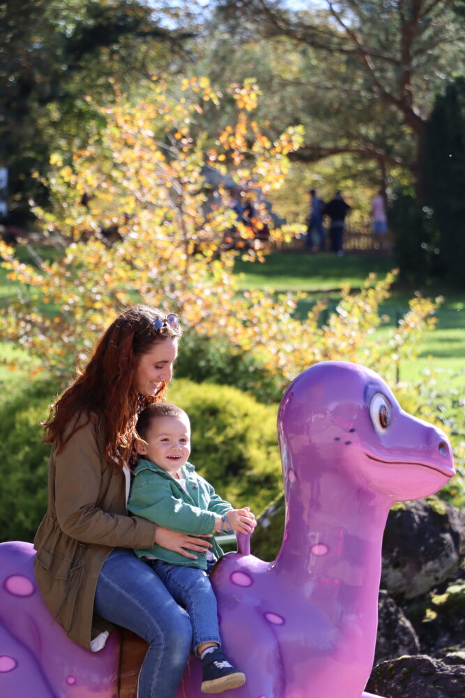 Femme et enfant sur un dinosaure dans l'attraction le Dino-Galopant