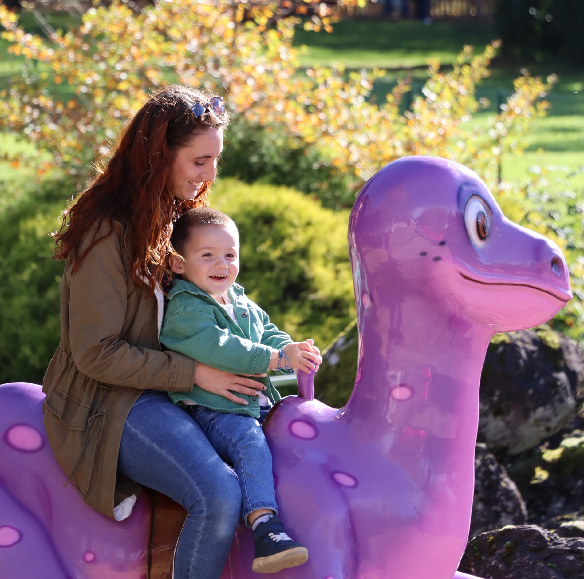 Femme et enfant sur un dinosaure dans l'attraction le Dino-Galopant